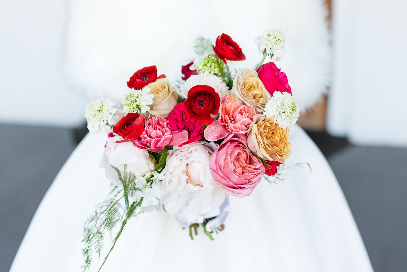 Bride holding a bouquet filled with roses, ranunculus, white pincushion, fresh ferns, and peonies