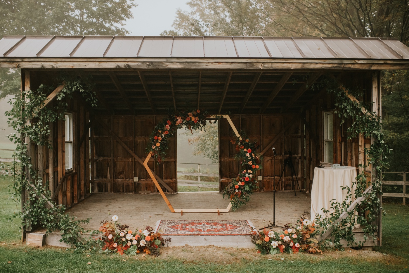 Burgundy, red, and peach flowers and a red oriental rug for a fall outdoor wedding ceremony