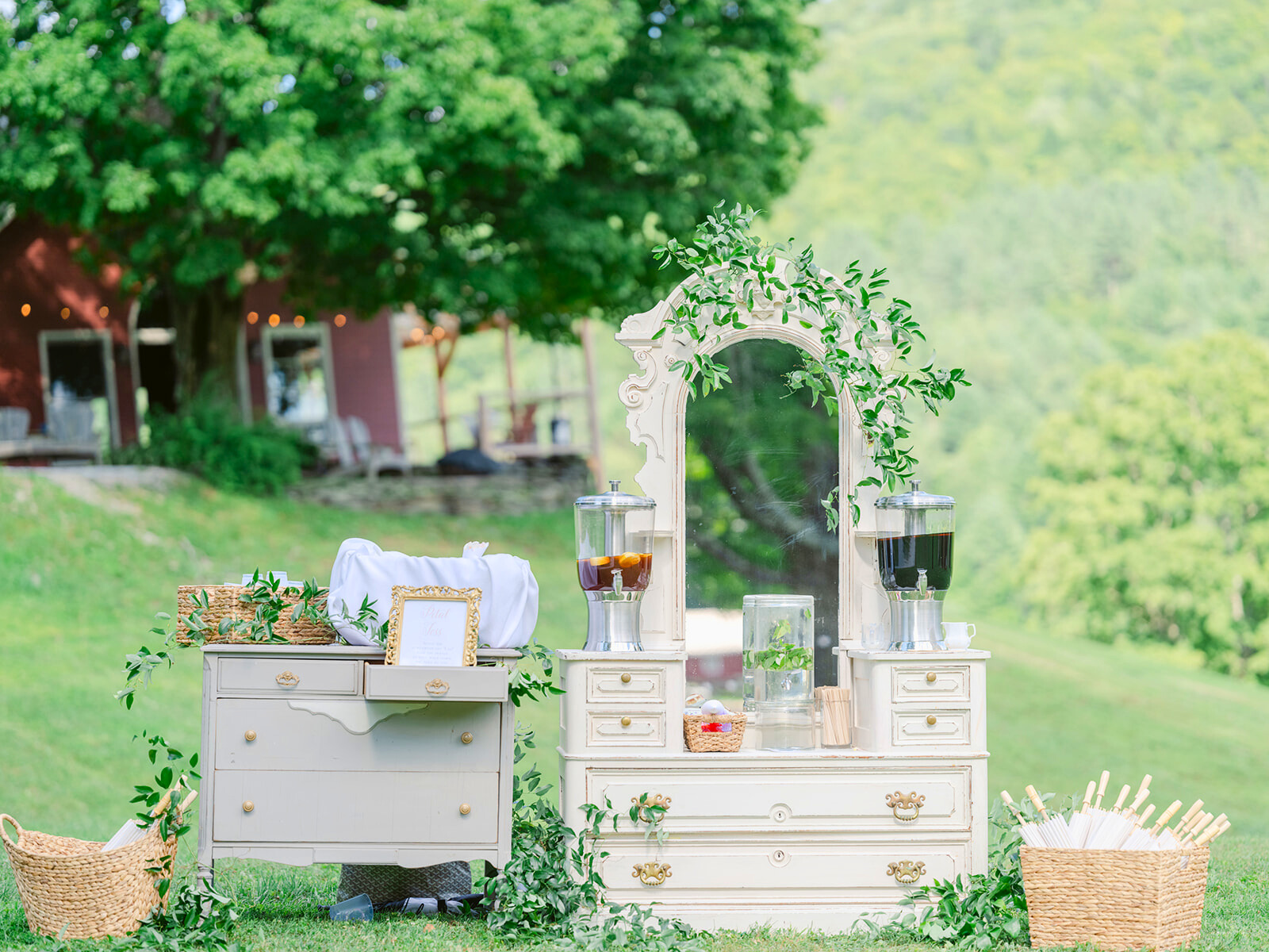 A vintage drink station with elegant white furniture, greenery, and baskets, showcasing Crystal & Oak's timeless rentals.